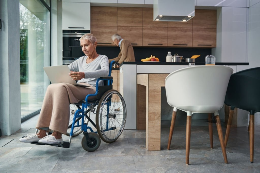 Senior woman using a wheelchair at home with a caregiver in the background